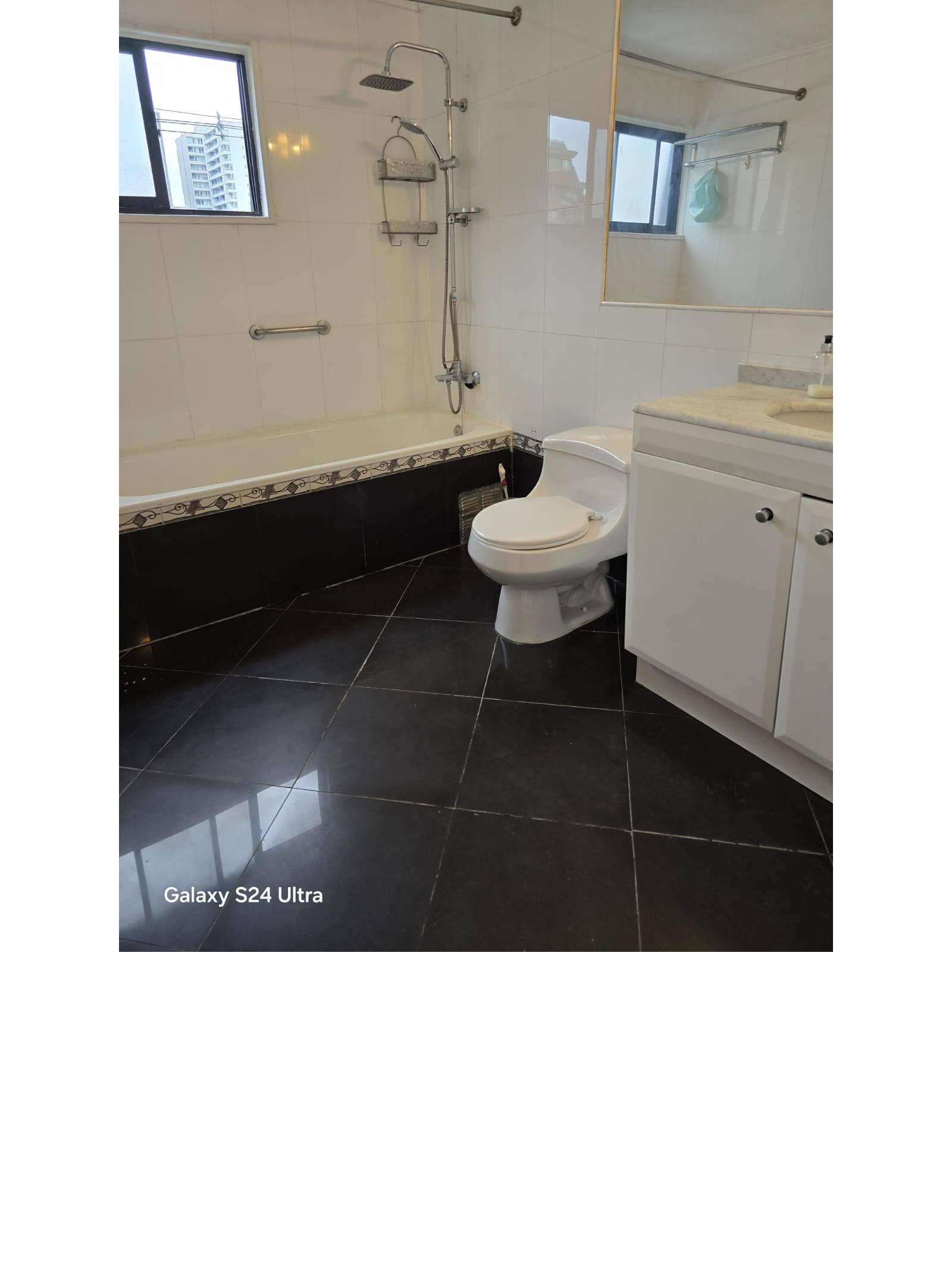 Baño con tina, sanitario, vanitorio y cerámica negra en piso.