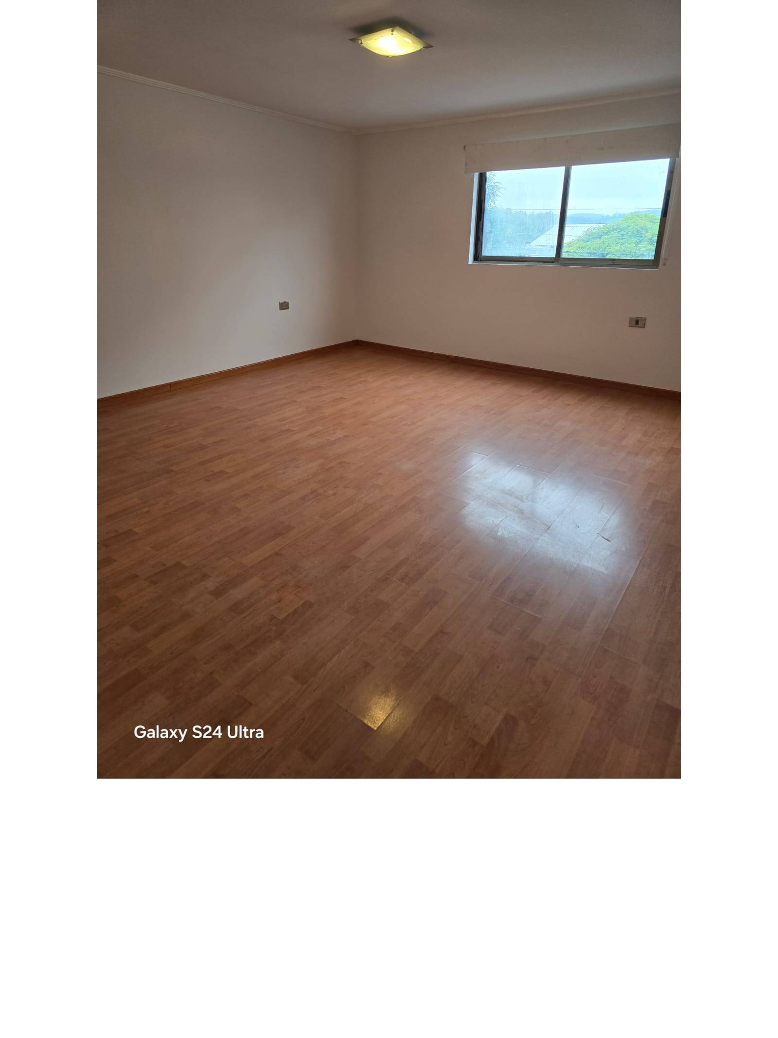 Dormitorio amplio con ventana y piso laminado brillante.