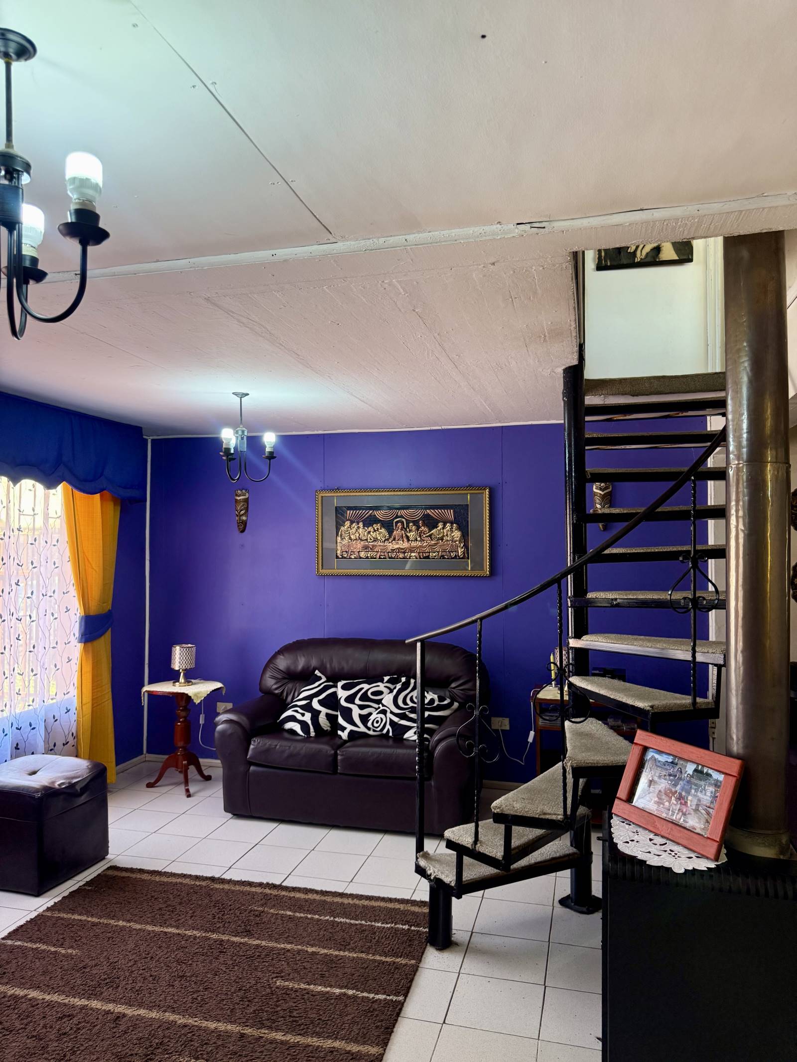 Living con muros morados, sillón oscuro y escalera de caracol.