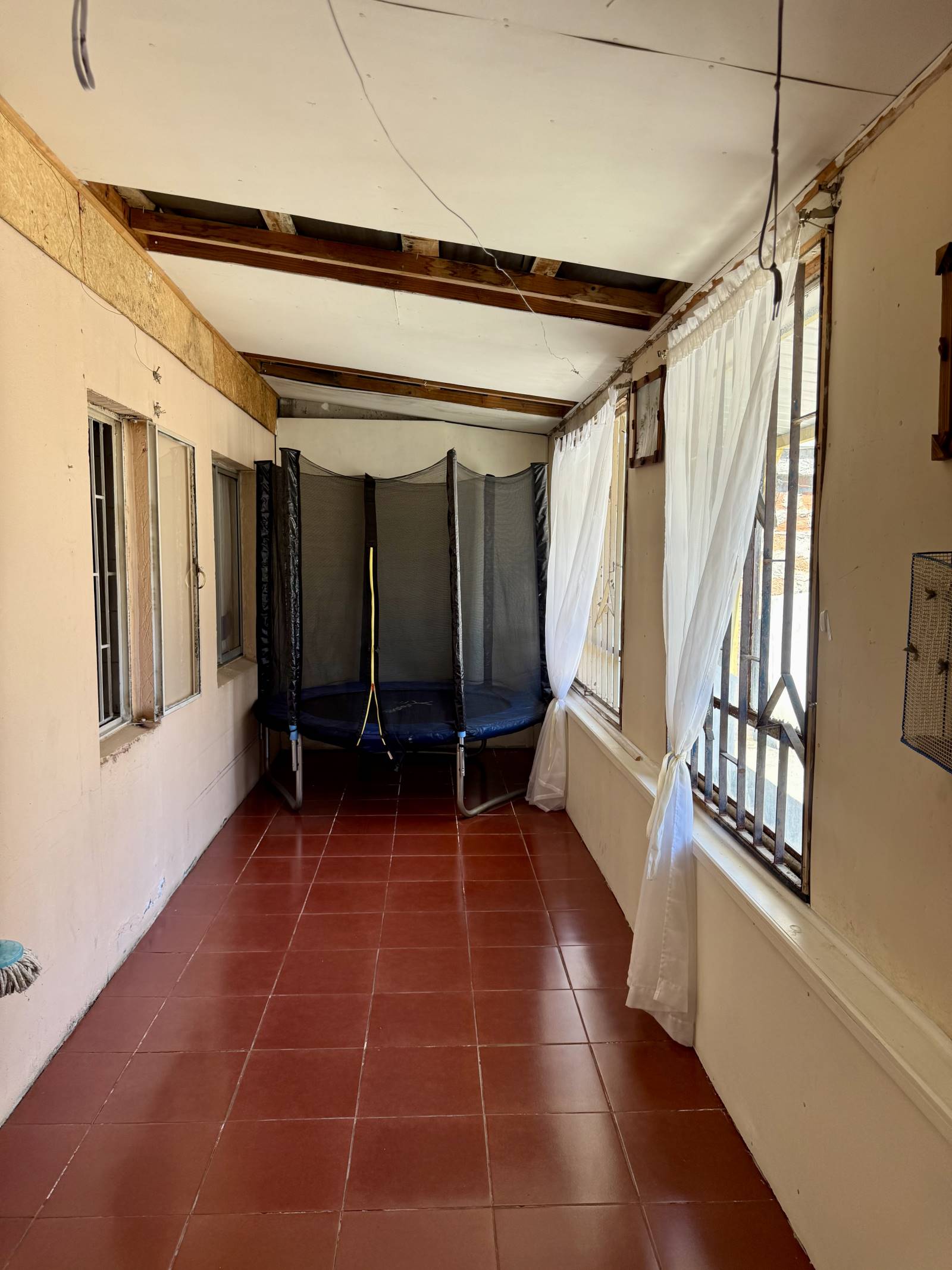 Galería techada con piso cerámico y cama elástica al fondo.
