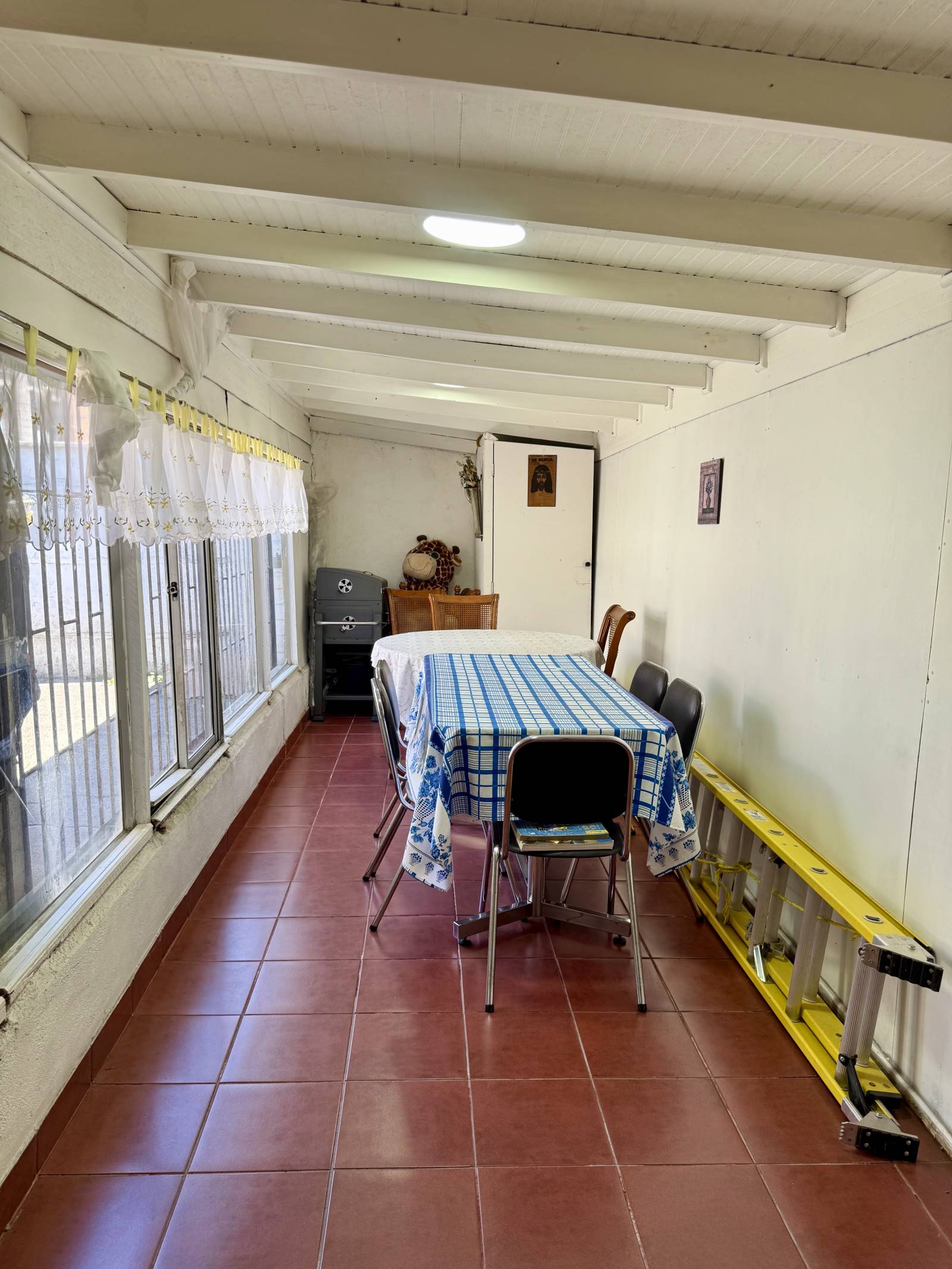 Galería cerrada con mesa de comedor y techo con vigas.