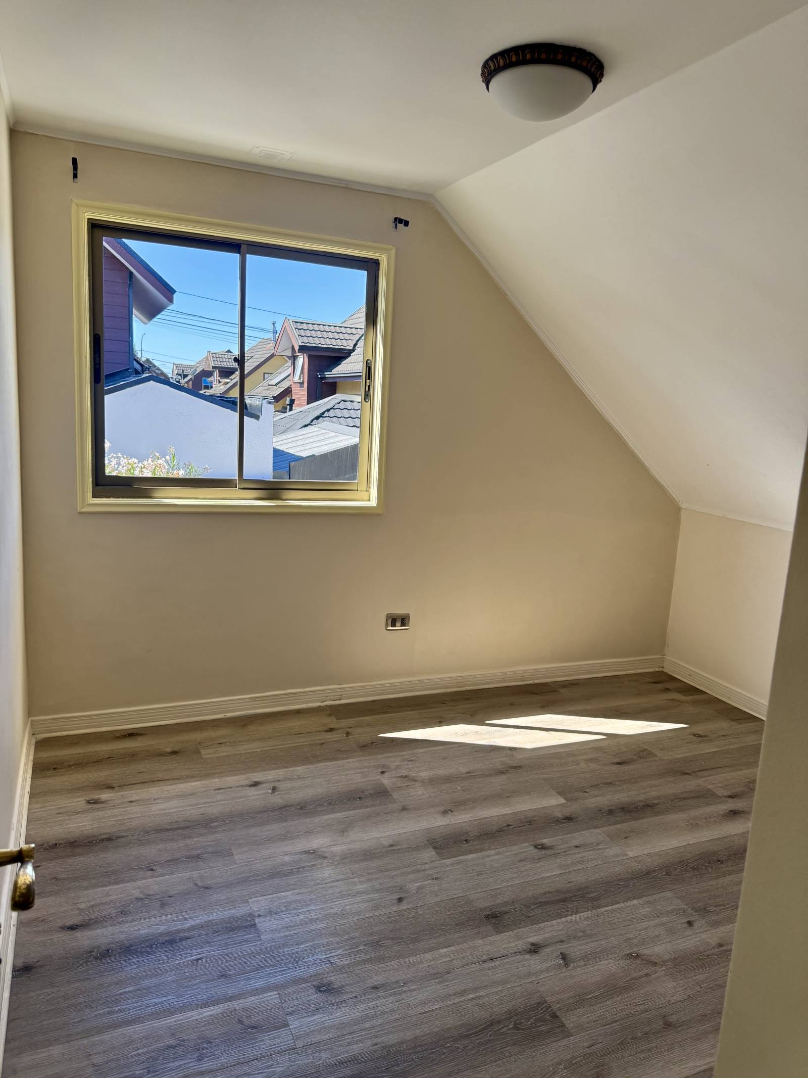 Dormitorio abuhardillado con piso flotante y ventana exterior.