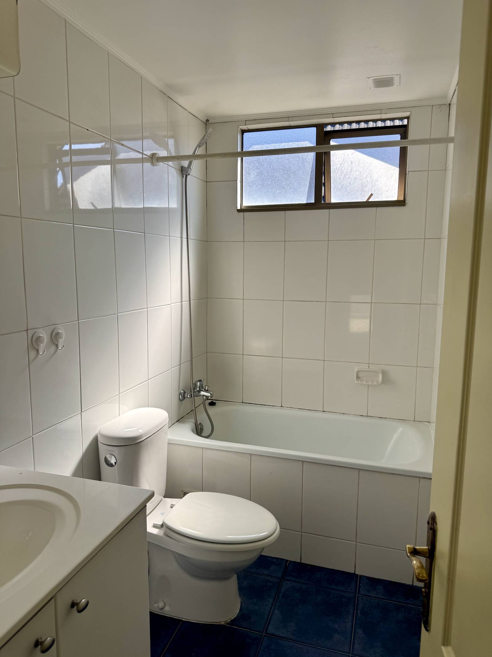 Baño completo con tina, cerámicos blancos y ventana de ventilación.