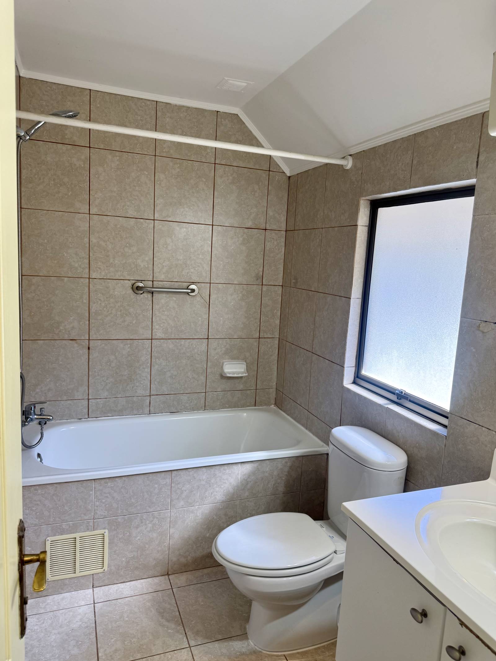 Segundo baño con tina, azulejos beige y ventana exterior.