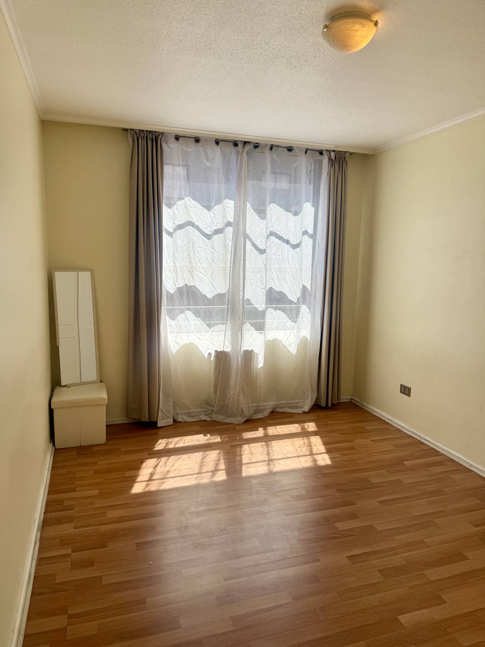 Dormitorio vacío iluminado con piso flotante y ventana con cortinas