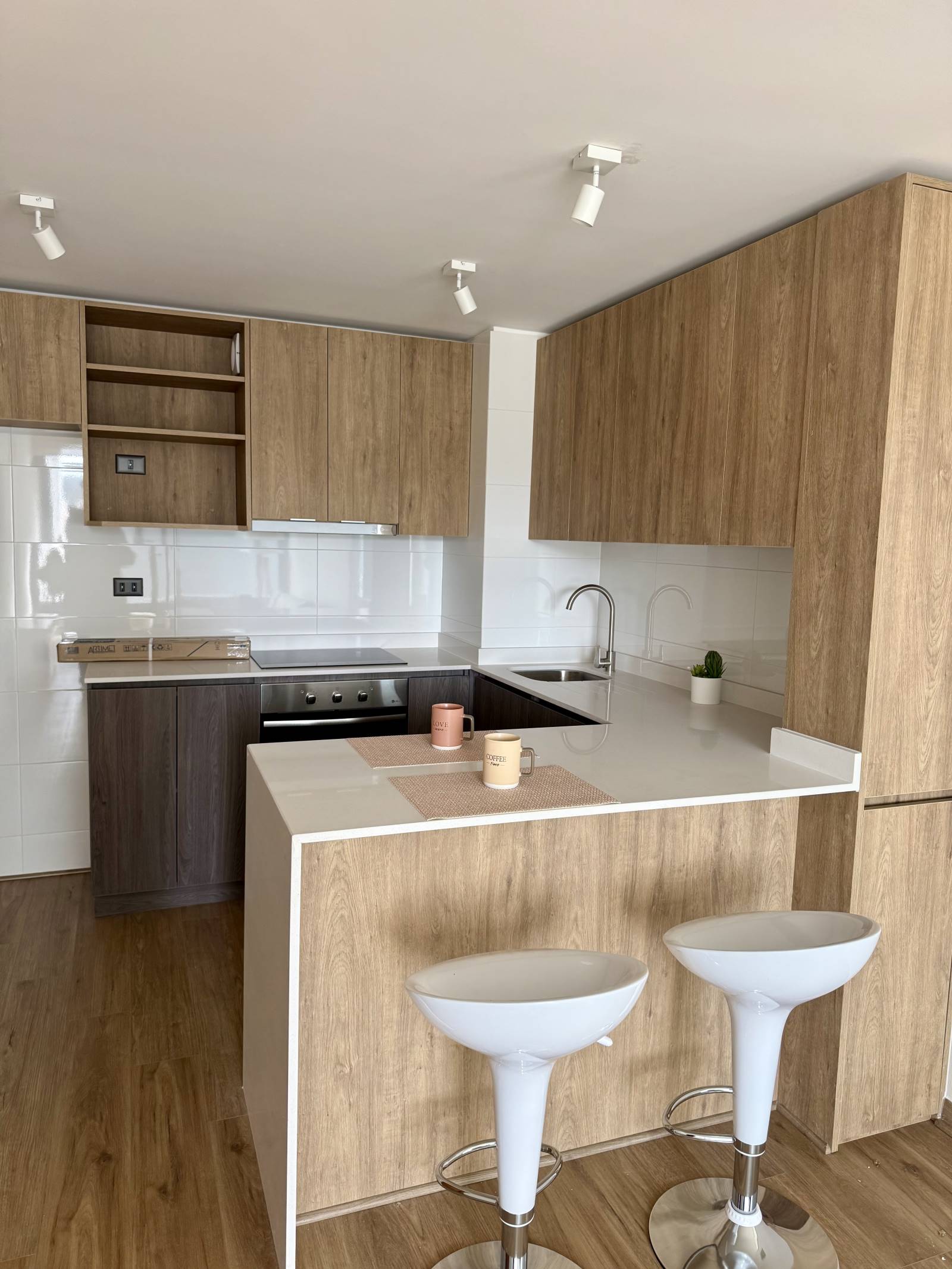 Cocina equipada con encimera, muebles en madera y barra con taburetes.