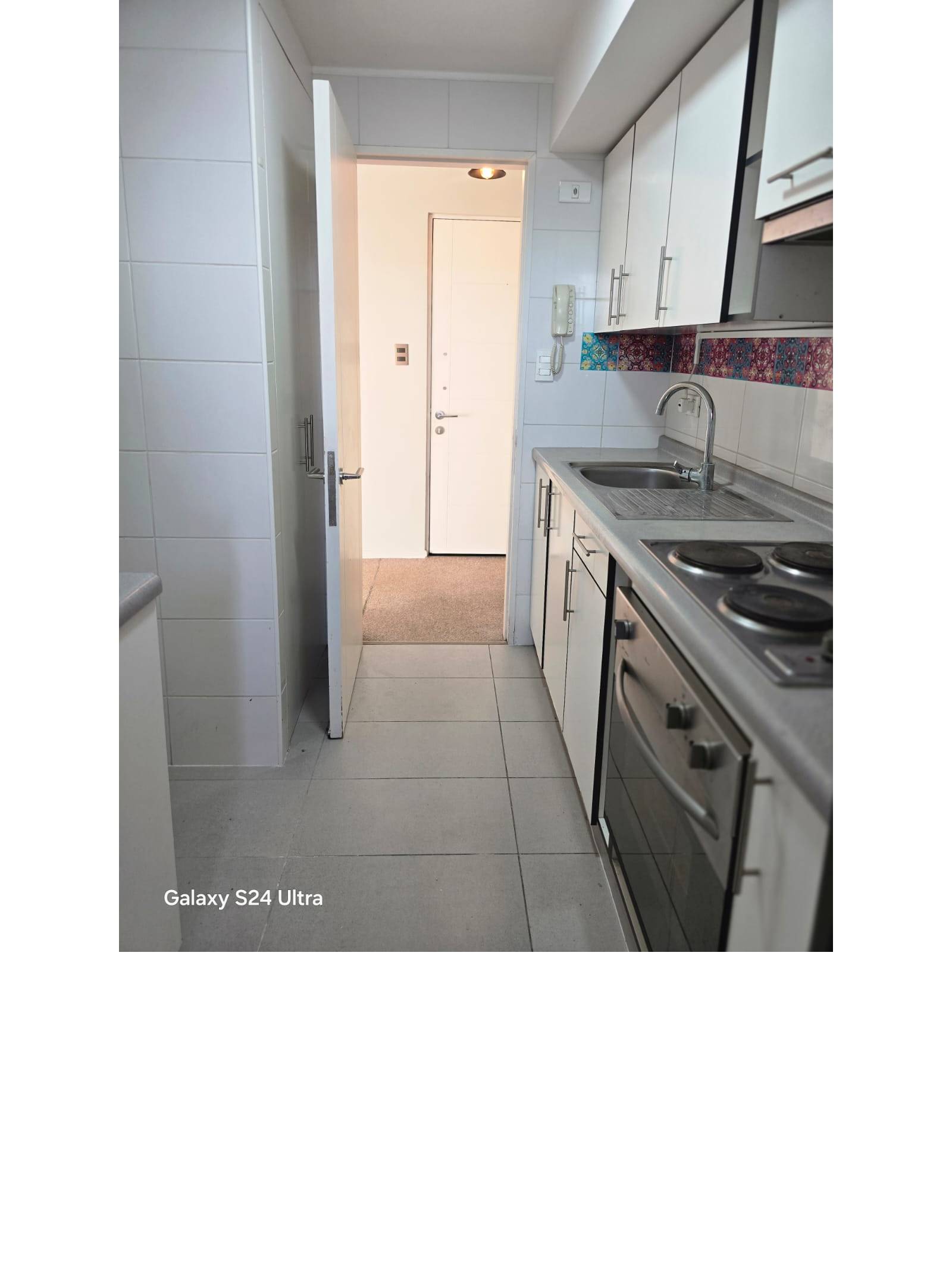 Cocina alargada equipada con encimera, horno y muebles blancos