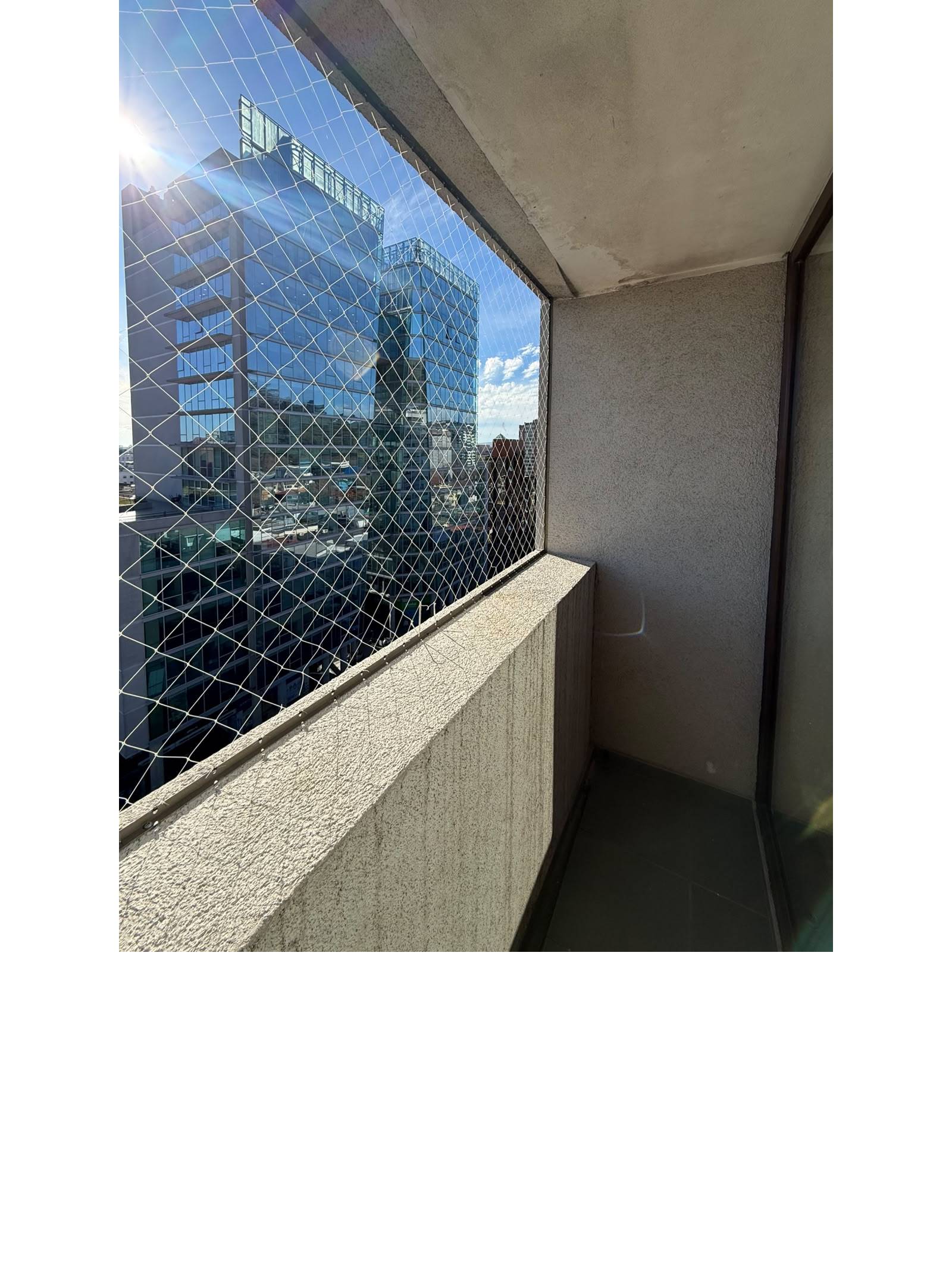 Balcón con malla de seguridad y vista a la ciudad.