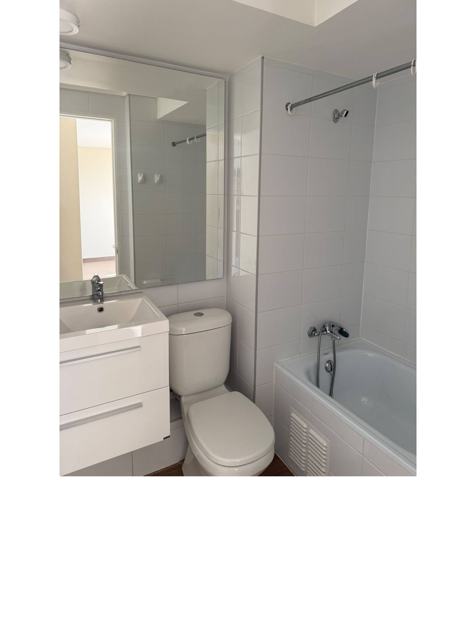 Baño con vanitorio blanco, inodoro y tina con ducha.