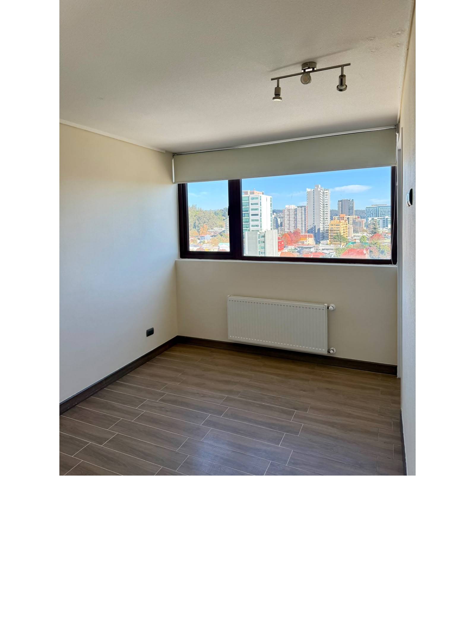 Dormitorio luminoso con radiador y amplia ventana a la ciudad.
