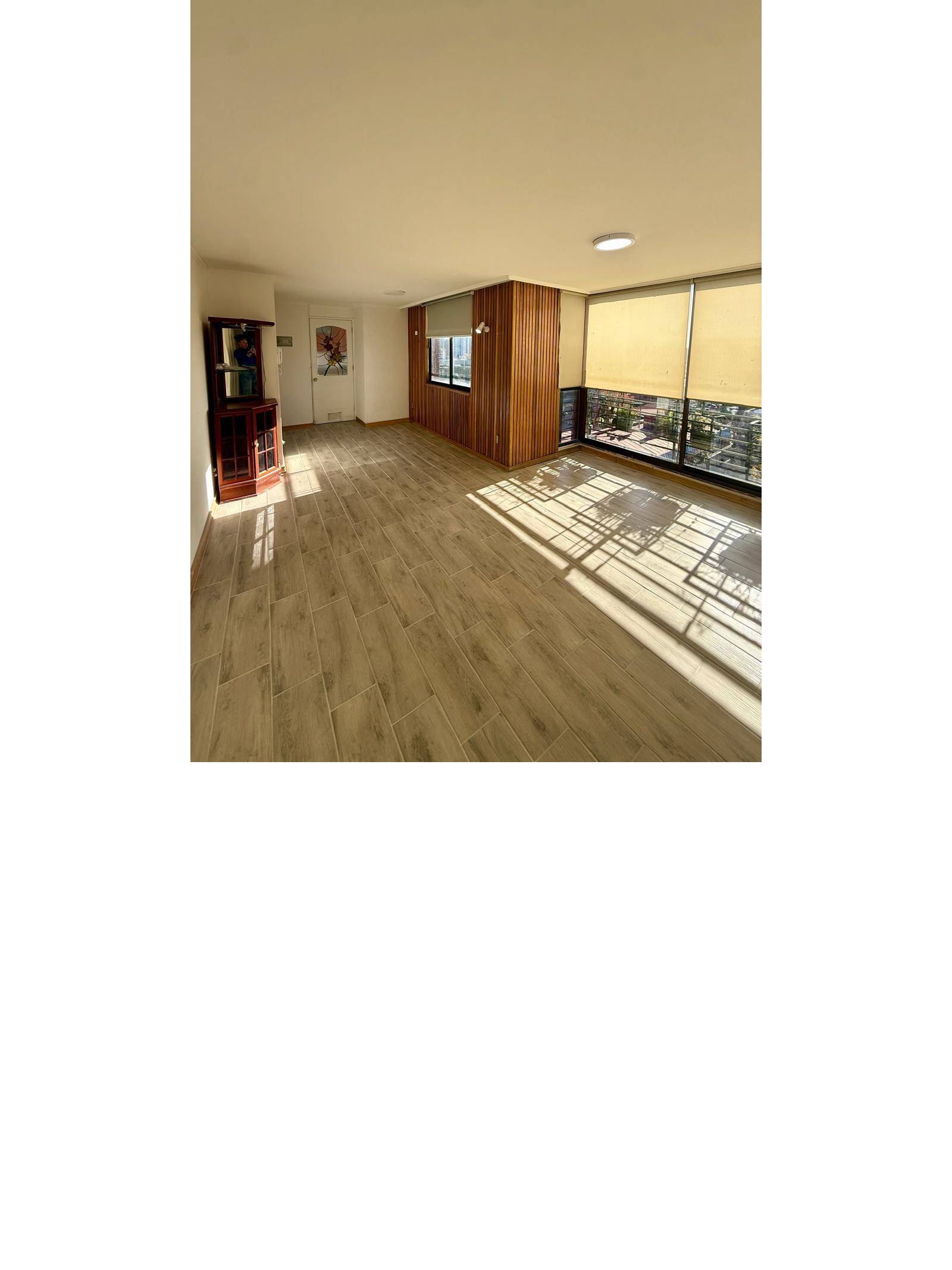 Living amplio con piso cerámico símil madera y grandes ventanales luminosos.