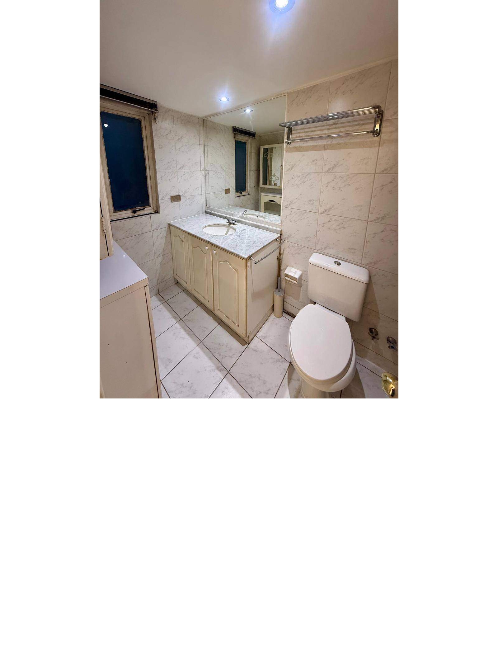 Baño completo con vanitorio de mármol, gran espejo e inodoro.