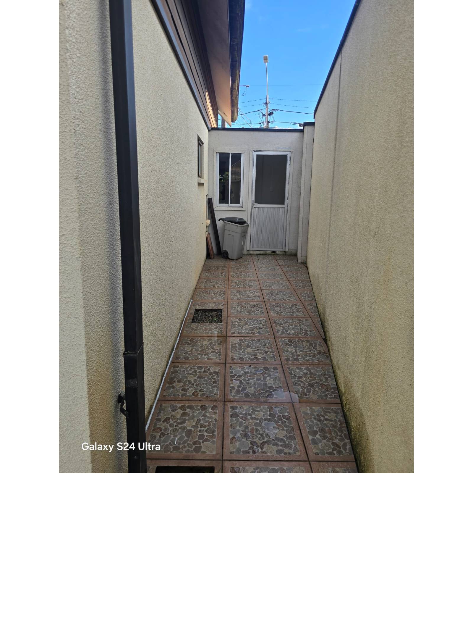 Pasillo lateral pavimentado hacia acceso posterior de la vivienda