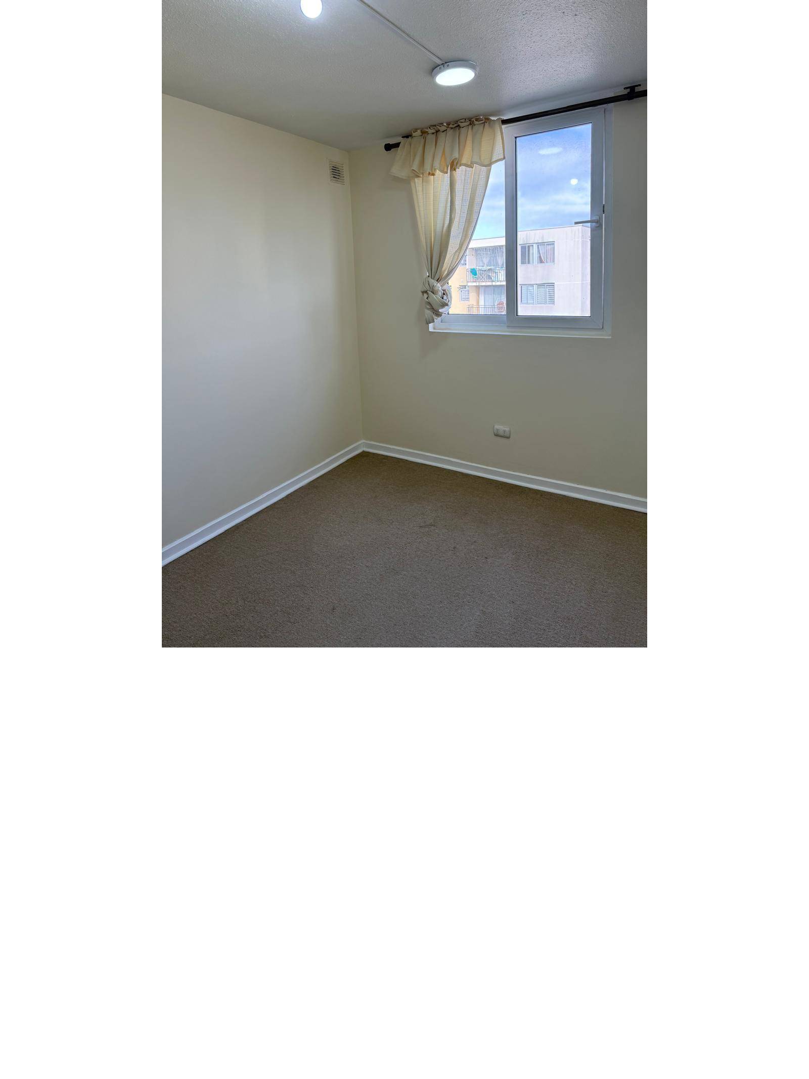 Habitación con piso alfombrado, ventana y muros claros.