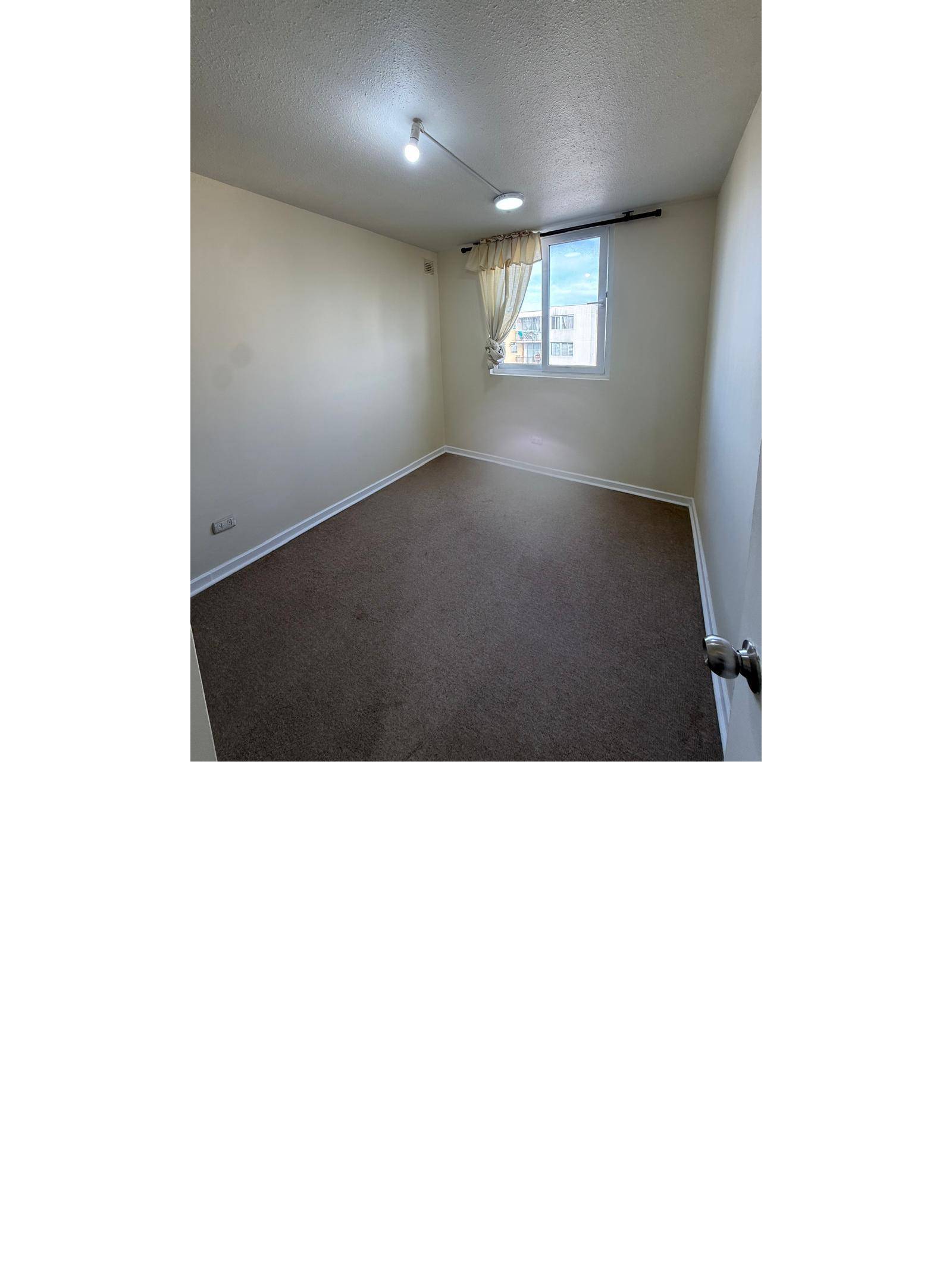 Dormitorio vacío con alfombra y ventana hacia patio interior.