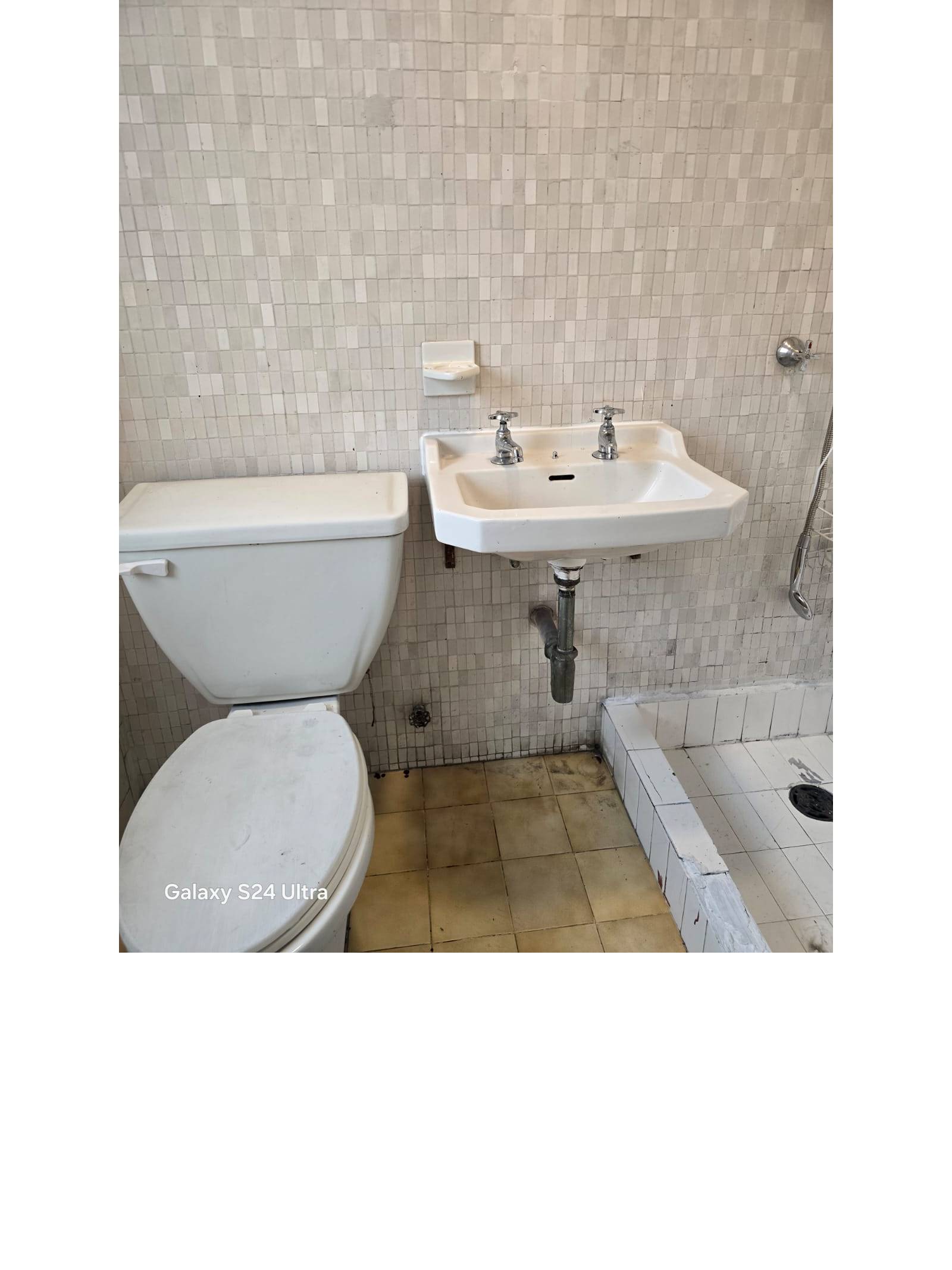Baño con inodoro lavamanos mural y paredes con azulejo