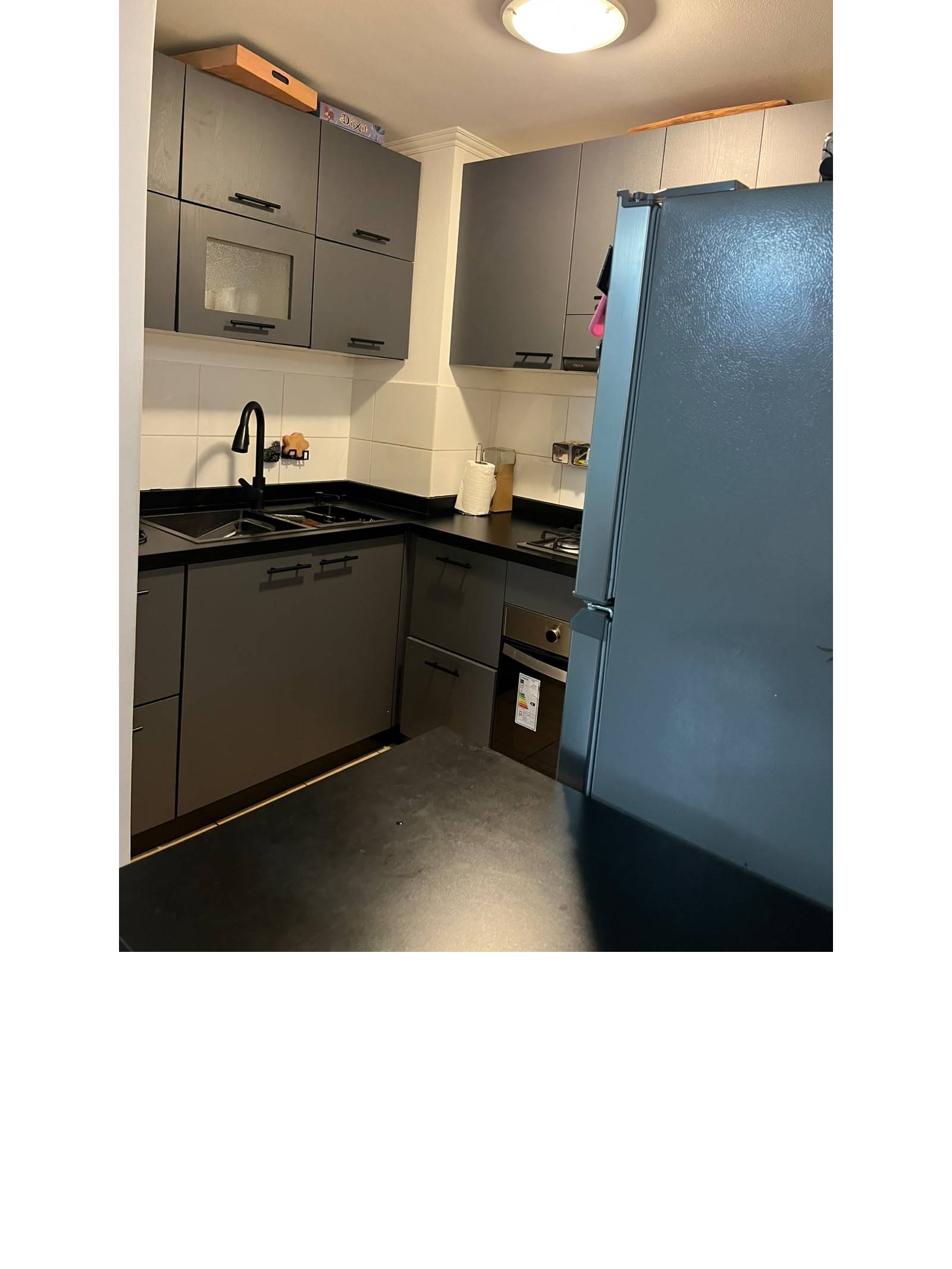 Cocina con muebles grises, cubierta negra y refrigerador