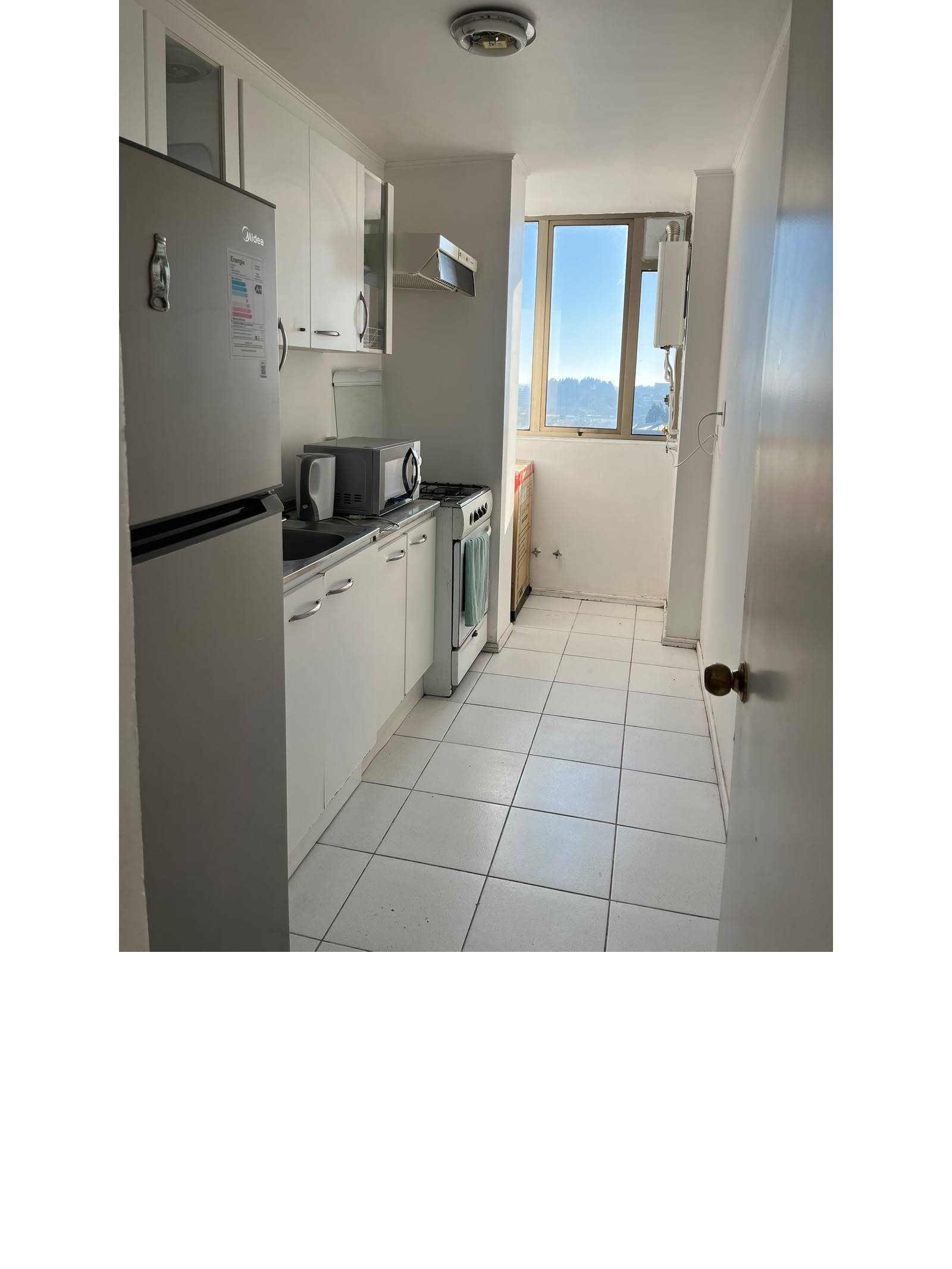 Cocina alargada amoblada con refrigerador, cocina a gas y ventana.