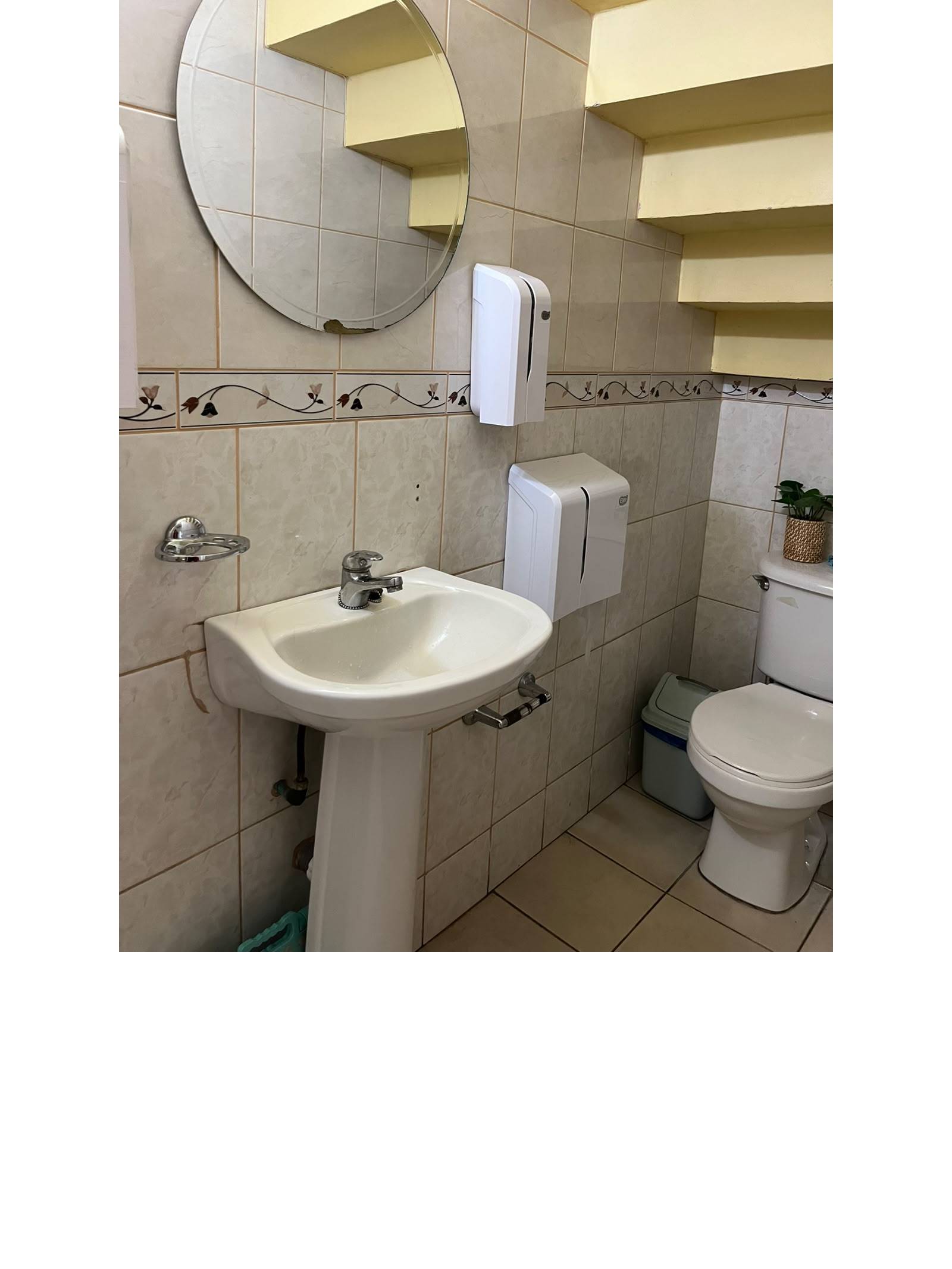 Baño con lavamanos de pedestal, espejo circular e inodoro.