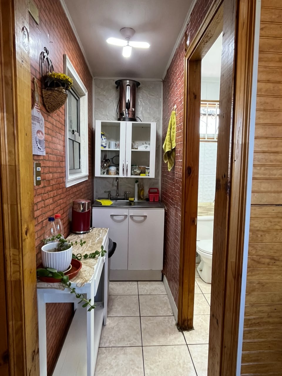 Kitchenette angosta con lavaplatos, mueble colgante y papel mural símil ladrillo