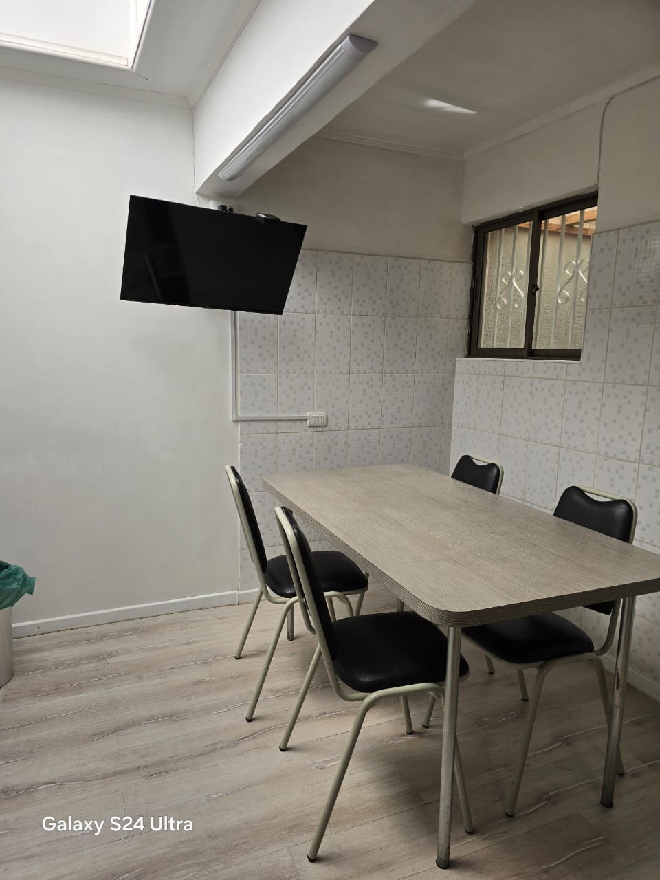 Comedor de diario con mesa clara, cuatro sillas y televisor mural.