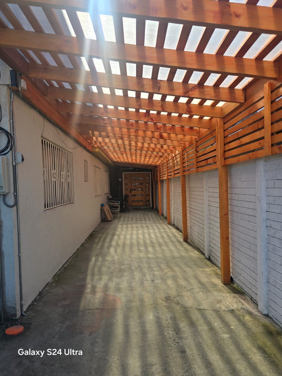 Estacionamiento techado longitudinal con estructura y vigas de madera.