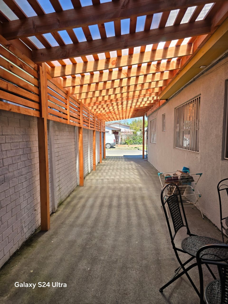 Entrada de vehículos techada con pérgola de madera hacia la calle.