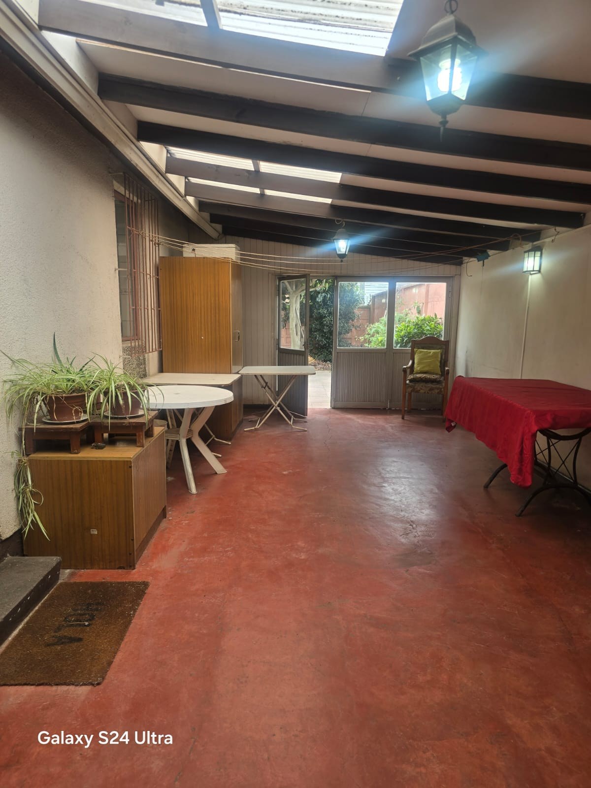 Galería techada amplia con piso cerámico rojo y vigas a la vista