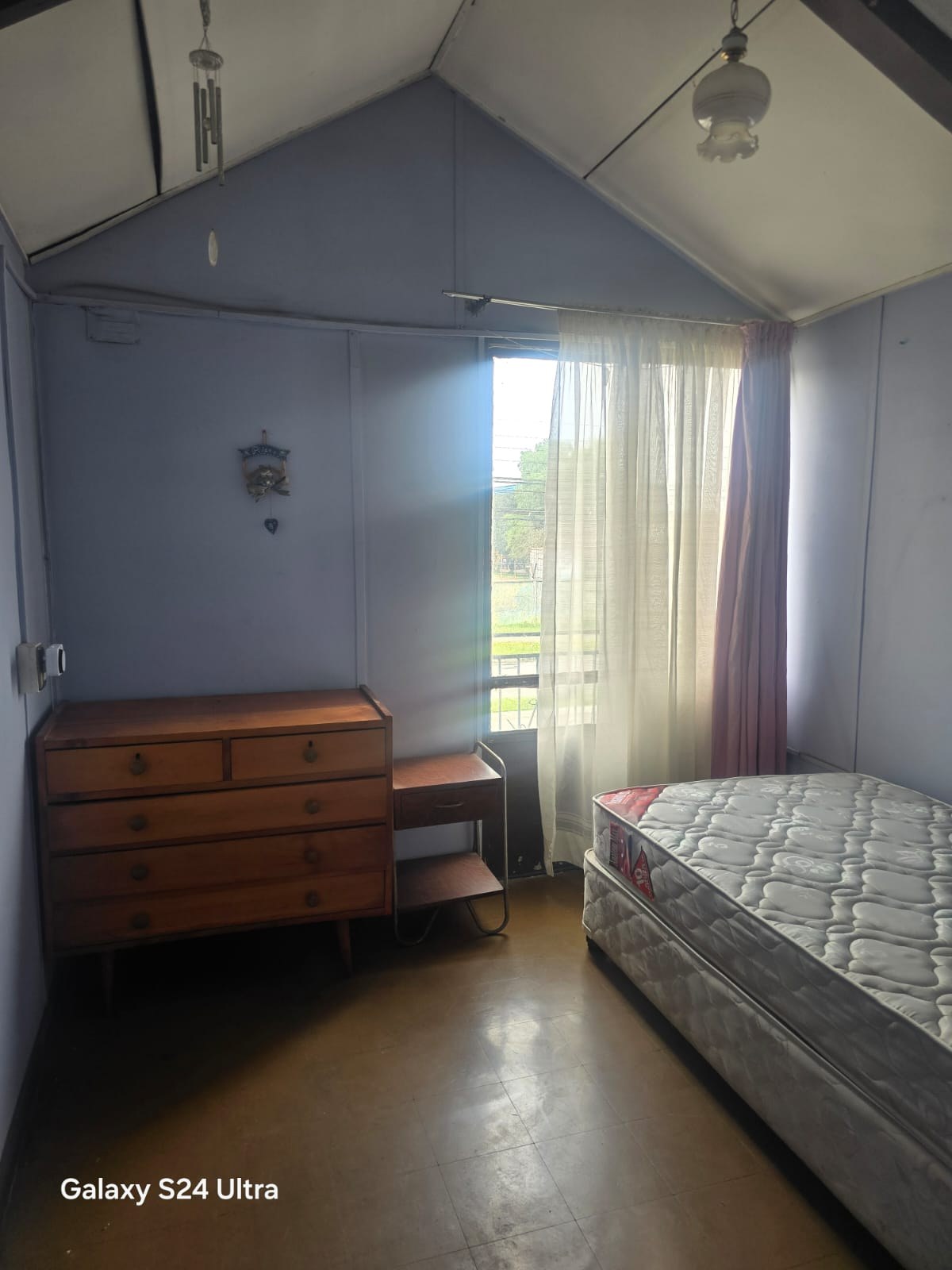 Dormitorio con techo inclinado, cómoda de madera y cama de plaza