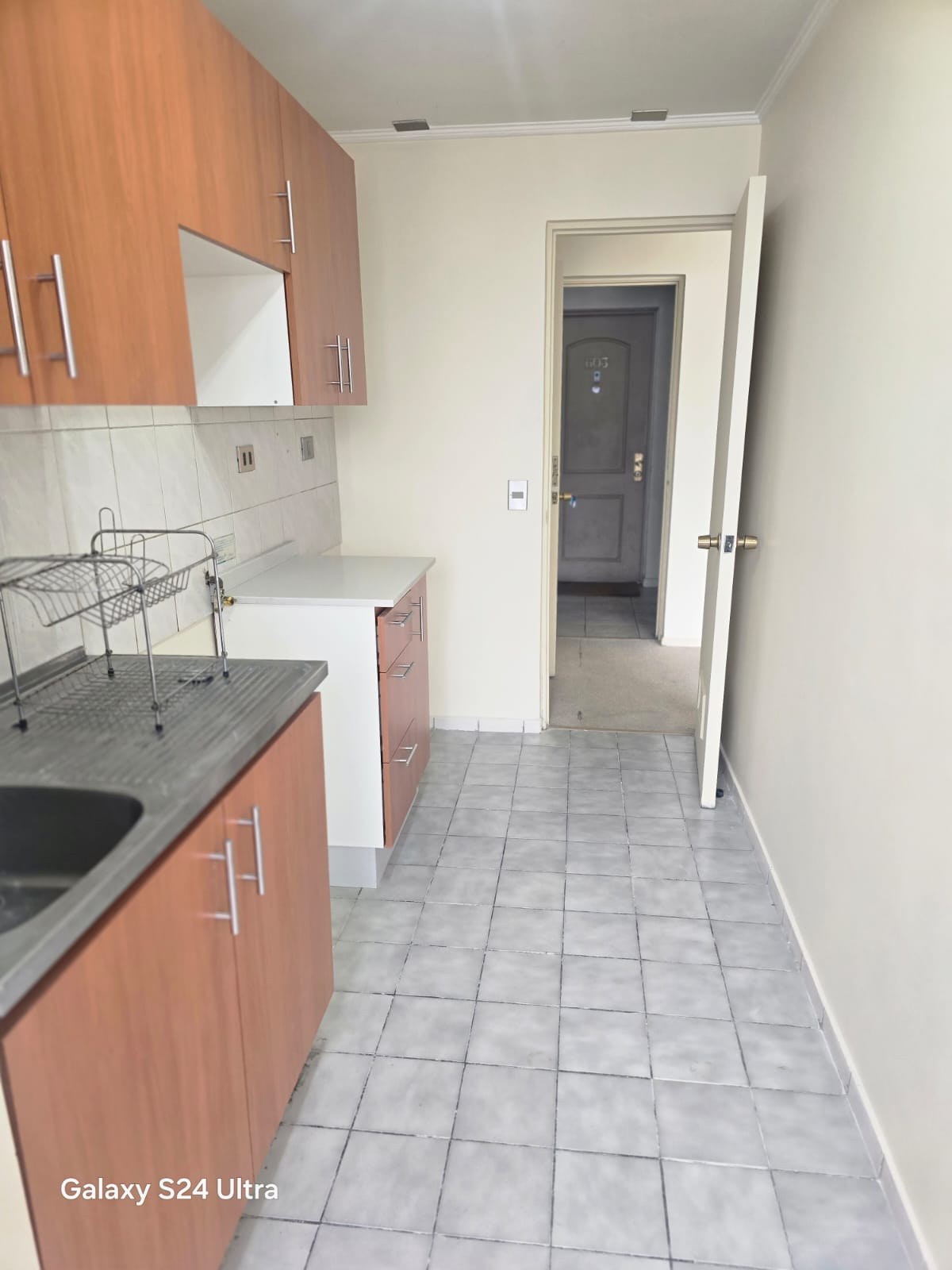 Cocina con muebles aéreos, encimera y puerta hacia pasillo