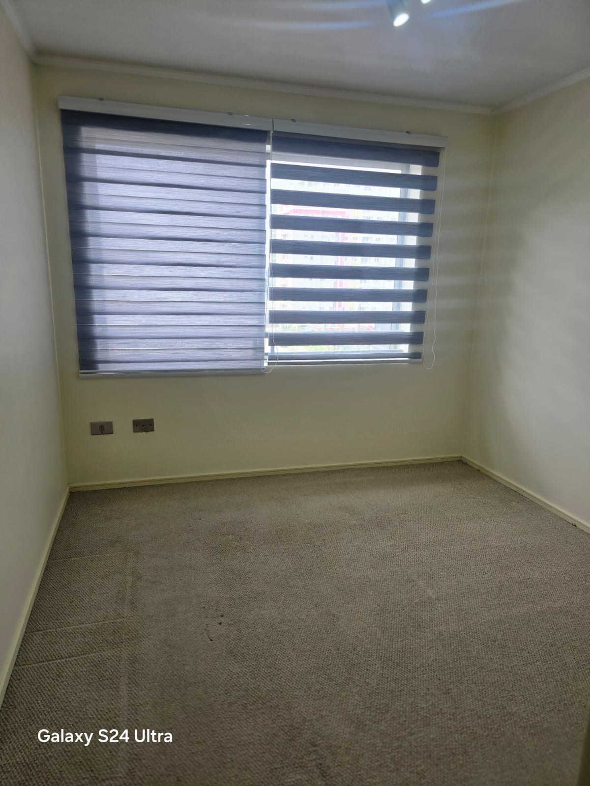 Dormitorio con piso alfombrado y ventana con cortinas roller
