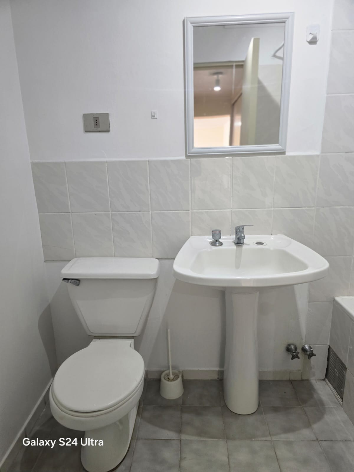 Baño con inodoro, lavamanos de pedestal, espejo y muros cerámicos