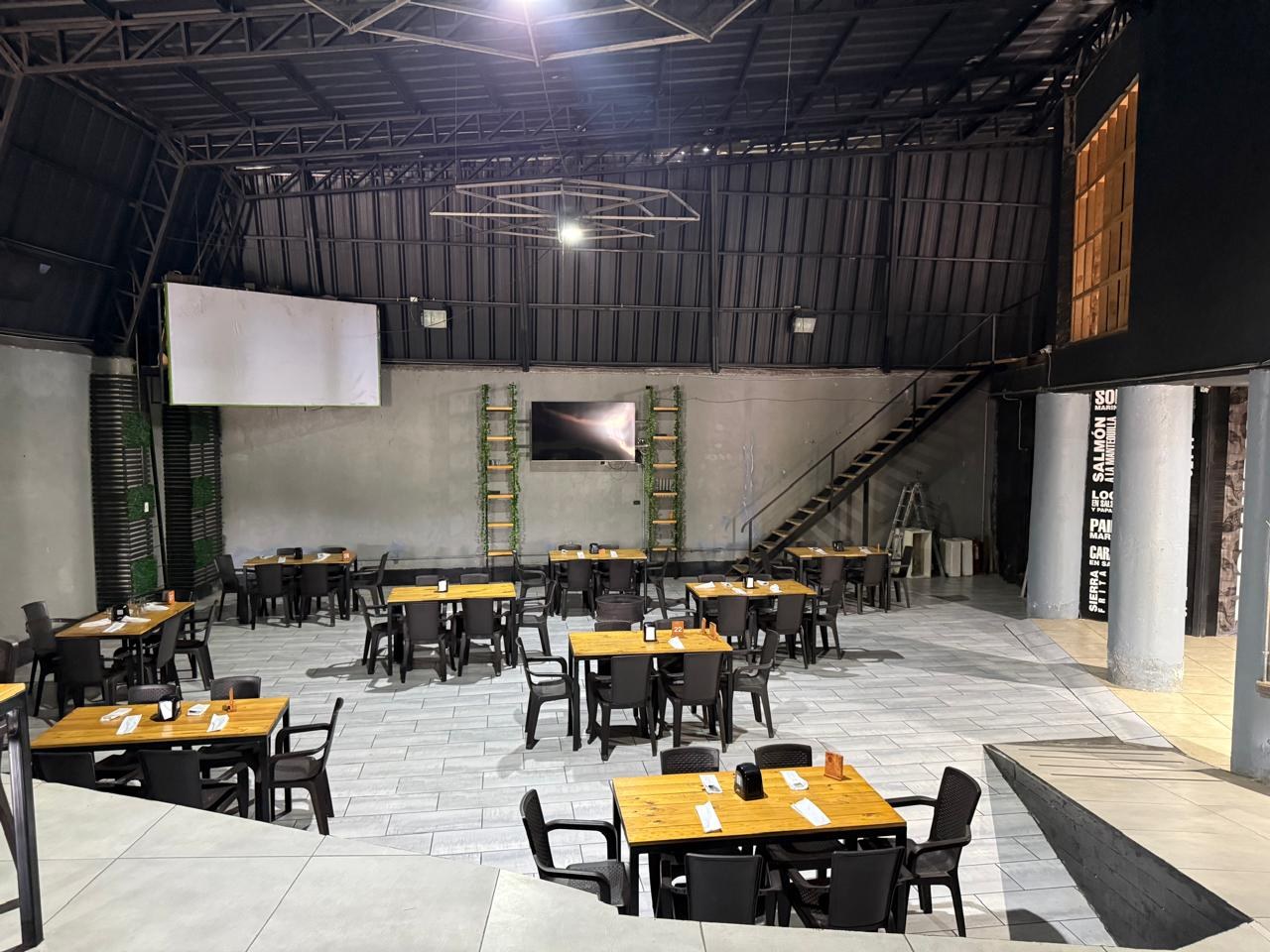 Salón principal amplio equipado con mesas, sillas y pantalla